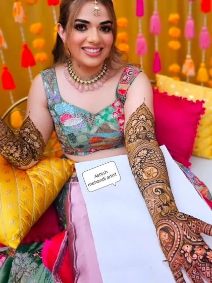 A happy bride posing with her full-arm mehandi during her vibrant mehandi ceremony.
