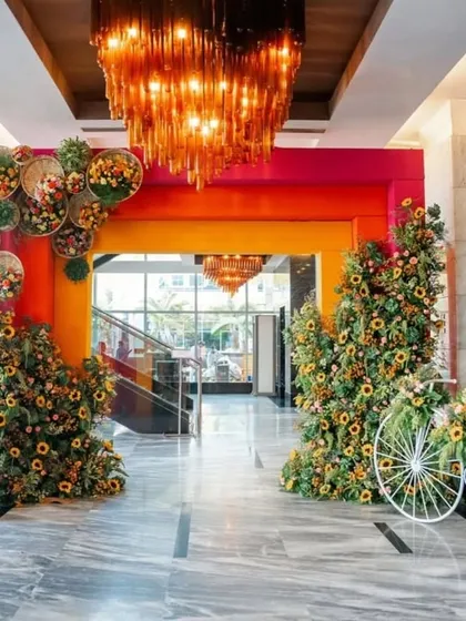 A grand entrance for a haldi ceremony. The colorful archway is flanked by large sunflower arrangements and a decorative bicycle, creating a warm and inviting welcome.