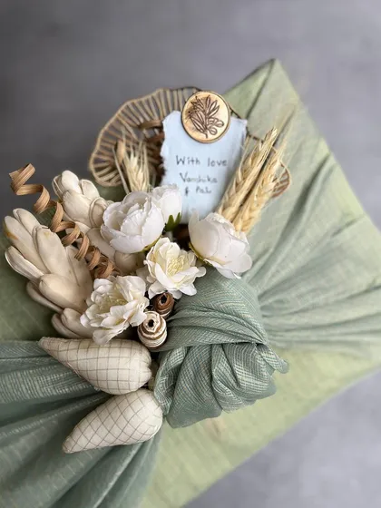 The art of Furoshiki, our sustainable fabric wrapping. This close-up shows a gift adorned with a bouquet of sola wood flowers and dried wheat, showcasing our commitment to beautiful, eco-friendly presentation.