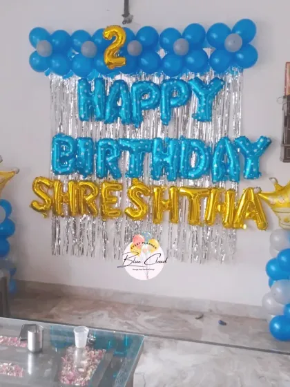 A royal-themed birthday wall decoration with blue and gold foil letters, a shimmer curtain, and crown-topped balloon pillars.