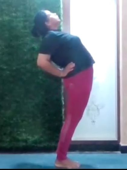 An instructor demonstrates a standing backbend, a preparatory pose for deeper backbends. We focus on building strength and flexibility progressively and safely in our online classes.