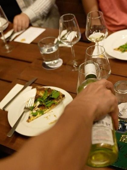 A guest pours a glass of crisp white wine to pair with a slice of our pizza during a tasting event.