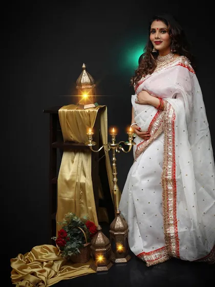 An eye-catching solo portrait of a mom-to-be in a beautiful white and red saree. She looks serene and graceful against the dark, traditionally styled set.