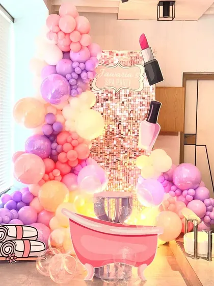 A full-length view of the spa party decoration, showcasing the impressive scale of the pastel balloon garland against the sequin backdrop. The fun, cartoonish props like the bathtub and rolled towels add a playful touch to the glam setup.