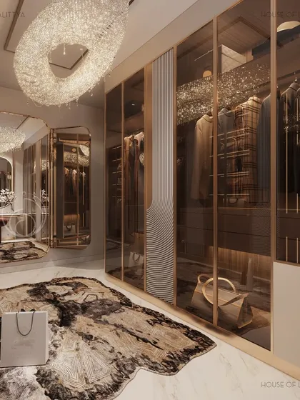 A closer view of the walk-in closet, highlighting the custom glass-fronted wardrobes with integrated lighting. The space is anchored by a statement rug and a large, ornate chandelier, making it a truly personal luxury.