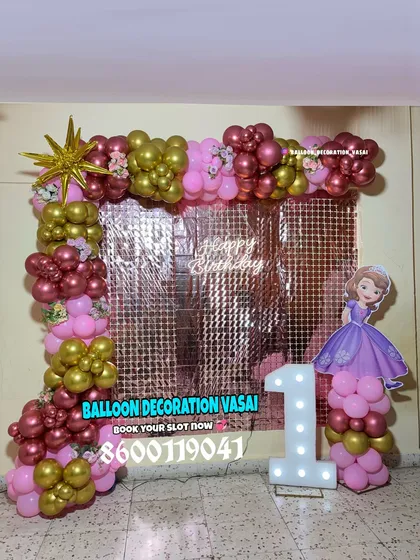 A royal first birthday party with a Princess Sofia theme. This decoration features a rose gold shimmer wall, a pink and gold balloon frame, and a Sofia the First cutout next to the marquee number.
