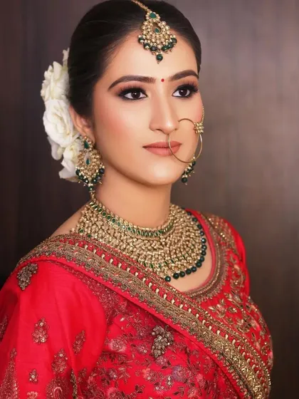 A stunning bridal portrait. The makeup features softly defined eyes and a clean base, complemented by a beautiful white floral bun and traditional jewelry for a look of pure elegance.