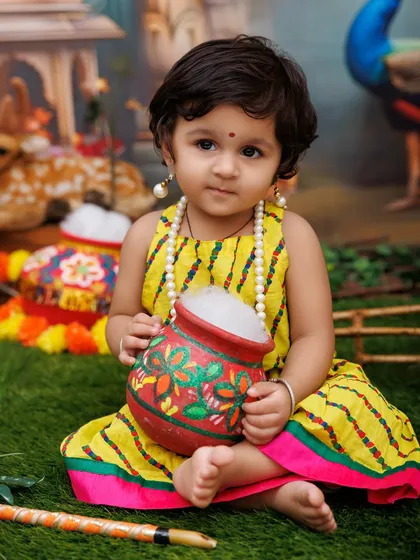 A close-up of a little Radha holding a painted makhan pot, with an innocent and curious expression.
