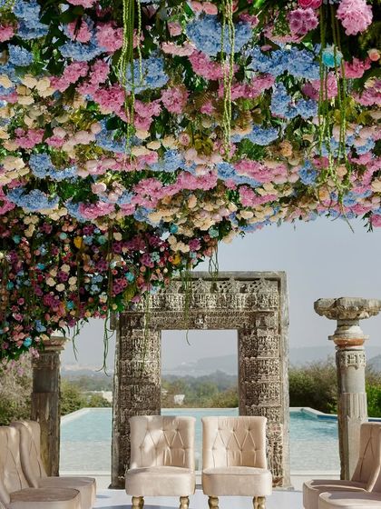 A detailed view of the pastel floral mandap, showcasing the intricate arrangement of hydrangeas and roses that form the canopy. The design integrates beautifully with the venue's existing stone architecture.