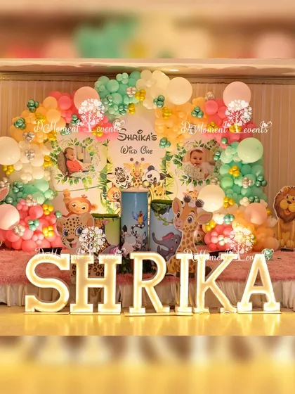 A clear, bright shot of the jungle-themed stage for "Shrika's Wild One" party. The pastel balloon arch and cute animal characters create a friendly and inviting atmosphere.