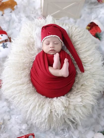 An adorable overhead shot of a baby swaddled in red, surrounded by classic Christmas props like Santa, a snowman, and a candy cane.
