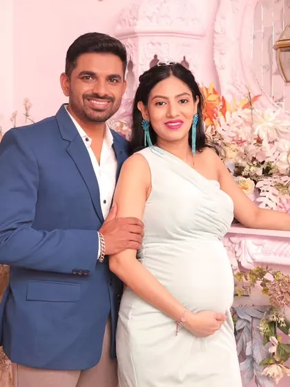 A happy couple portrait from a maternity photoshoot. The pastel pink background, combined with the vibrant floral decor, provides a cheerful and romantic setting to celebrate the upcoming arrival.