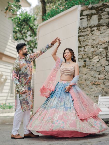 The groom twirls his bride during their Mehendi photoshoot. The movement of her multi-colored lehenga and their happy faces create a vibrant and joyful image.