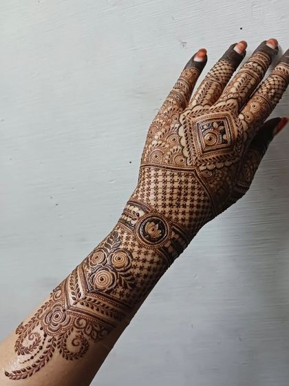 A complete view of an intricate back-hand design that extends up the arm. The pattern flows from a central geometric element, using a mix of grids and traditional motifs for a stunning effect.