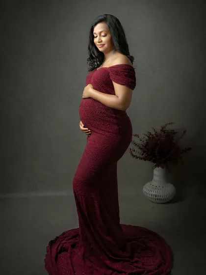 A classic portrait is always in style. This stunning mom-to-be in a form-fitting deep red gown against a simple, dark backdrop showcases her beautiful baby bump with elegance and confidence.