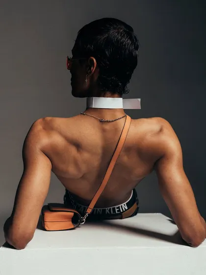 A full back view for a Calvin Klein accessories campaign. The pose and lighting are designed to draw attention to the bag and the defined musculature of the model.