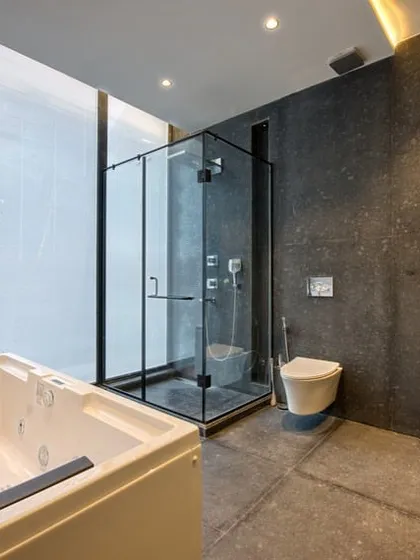 This bathroom combines a jacuzzi tub and a glass-enclosed shower. The large window allows for natural light, while the dark stone tiles create a grounded, earthy feel.