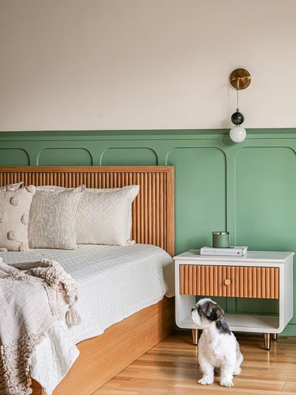 Another angle of the green and wood bedroom, highlighting the modern wall-mounted light fixture and the soft, textured pillows that add a cozy touch.
