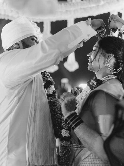A sacred moment during the wedding ceremony, captured in timeless black and white. The focus is on the couple's interaction, their hands, and their expressions, creating an intimate feel.