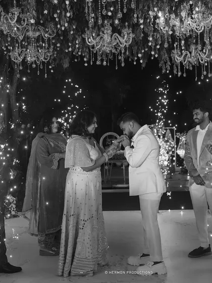 A timeless black and white shot of the groom kissing his bride's hand on the dance floor, surrounded by fairy lights.