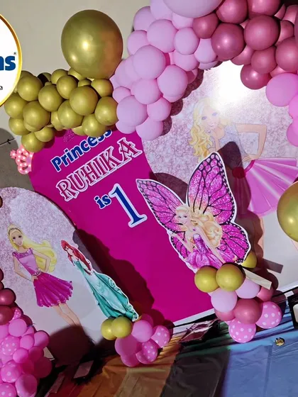 A close-up of a princess-themed first birthday backdrop, featuring Barbie and a large butterfly.
