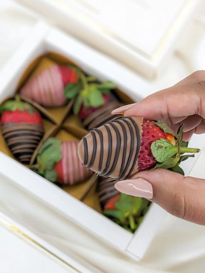 A close-up of a hand-picked, perfectly drizzled chocolate-coated strawberry, showcasing the quality and freshness.