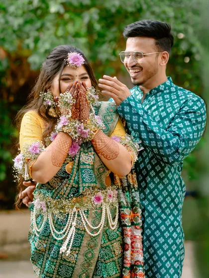 A joyful, candid moment from a traditional baby shower. The couple's laughter is infectious, and the bride-to-be looks radiant in her green saree and floral jewellery.