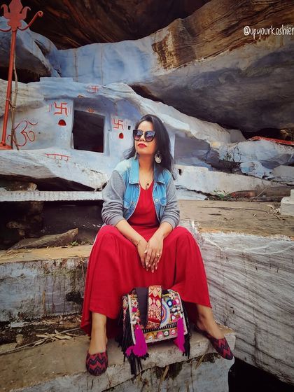 A vibrant red jumpsuit paired with a denim jacket and embroidered accessories creates a unique, bohemian travel look.
