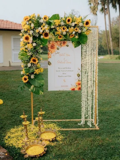 For this outdoor Haldi ceremony, we created a welcoming entrance that blends modern design with tradition. The custom sign is framed by an arc of fresh sunflowers and delicate jasmine strings, with brass lamps adding a customary touch.