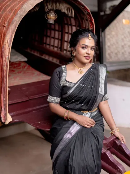 A full-length shot of the model in a traditional setting. The black saree and gold jewelry look stunning against her glowing skin.