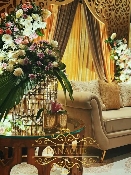 A close-up of a floral centerpiece on a side table, featuring a birdcage element filled with flowers. This adds a touch of whimsy to the sophisticated gold-themed decor.