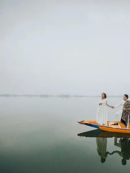 A wide shot of the couple on a traditional Shikara, seemingly floating on the calm, reflective waters. This image captures the peace and tranquility of a destination shoot in Kashmir.