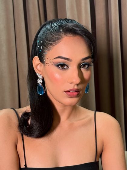 A close up of this blue-toned party look. The rhinestones scattered along the hairline and cheekbone add a unique, celestial touch to the classic winged eyeliner and smokey shadow.