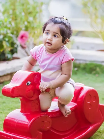 A cute candid of a baby girl playing on a red rocking horse in a garden. This photo captures a moment of discovery and play during a family shoot.