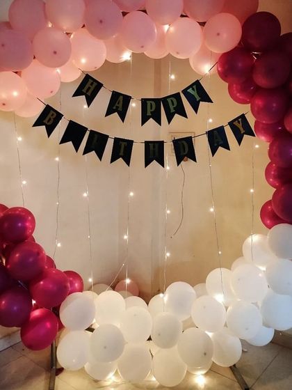 A simple yet beautiful setup for a birthday celebration. This design features a metal ring frame decorated with pink, maroon, and white balloons, with a classic 'Happy Birthday' banner strung across the center and accented with delicate fairy lights.