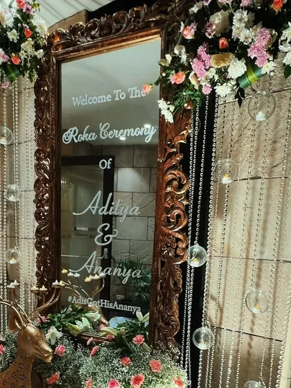 An ornate, vintage-style mirror serves as a welcome sign, adorned with hanging crystal beads and lush floral arrangements for a touch of old-world charm.