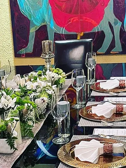 An impeccably set table for a formal dinner at home, featuring gold charger plates, crisp white linens, and elegant floral arrangements.
