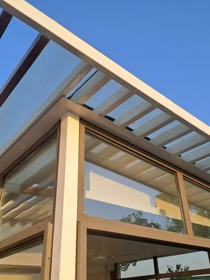 An upward-looking shot of a sunroom corner, highlighting the clean lines of the white steel frame against a clear blue sky. We focus on precise joinery to ensure a sleek, modern, and weatherproof finish.