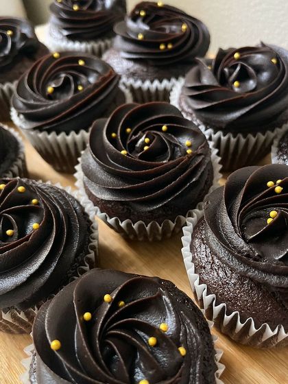 A close-up of our decadent chocolate cupcakes. The perfectly piped frosting and gold bead sprinkles add a touch of luxury to these popular party treats.