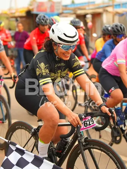 A female rider from the Cyclology team, smiling as she crosses the finish line.