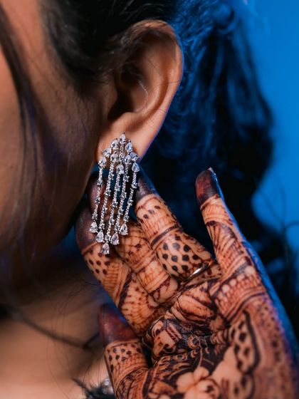 A close-up on the bride's stunning diamond earring, with her intricate henna-adorned hand in the frame. We focus on the jewelry and details that complete your look.