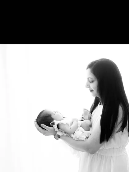 A black and white portrait of a mother holding her newborn. The high-key lighting and monochrome effect create a timeless and artistic feel, focusing on the silhouette and emotion.
