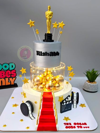 A glamorous two-tier Oscar-themed cake with a red carpet, film reel, and a custom 3D-printed Oscar trophy.