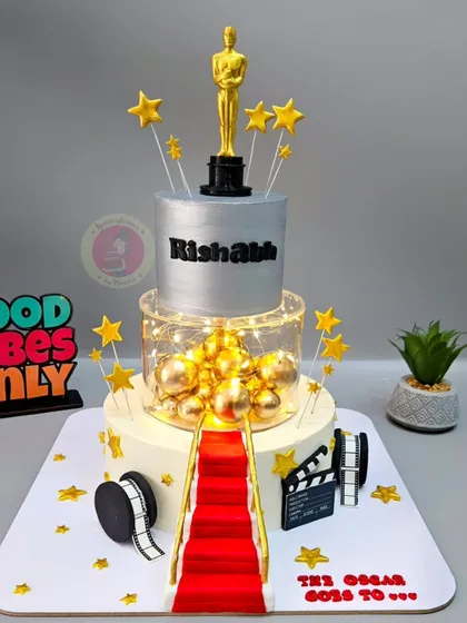 A glamorous two-tier Oscar-themed cake with a red carpet, film reel, and a custom 3D-printed Oscar trophy.