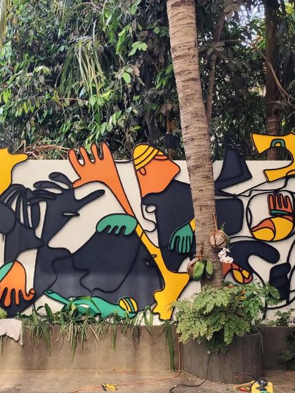 The nearly completed outdoor mural, with its vibrant yellow, orange, and green elements attached, nestled among the lush greenery.