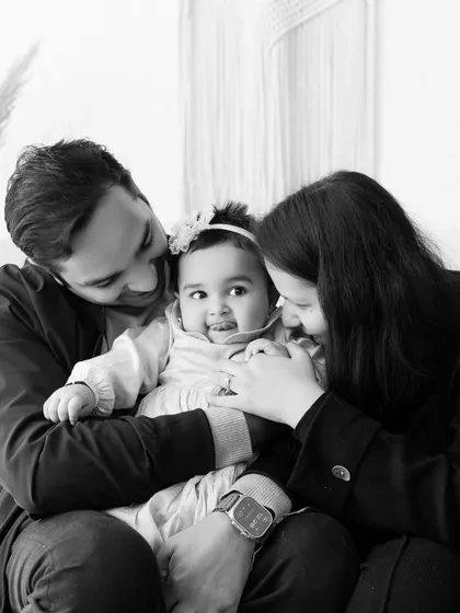 An intimate black and white portrait of a family cuddling their baby. The focus is entirely on their loving interaction and gentle touch.