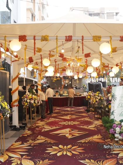 A grand entrance for a daytime Mehendi ceremony. We used a beautiful patterned carpet runner, floral arrangements on pedestals, and a ceiling decorated with hanging lanterns and marigold strings.