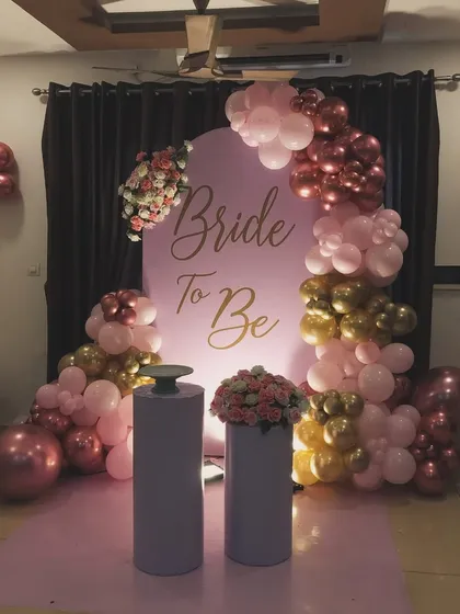 This is a chic bridal shower decoration I created using a popular pink chiara panel backdrop with custom gold 'Bride To Be' lettering. The look is completed with an organic balloon garland in shades of pink, gold, and maroon, and plinths for the cake and floral arrangements.