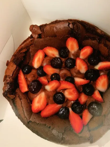 A close-up of my flourless chocolate cake, packed and ready to go. Topped with fresh strawberries and blueberries, it's a rich and decadent gluten-free option.