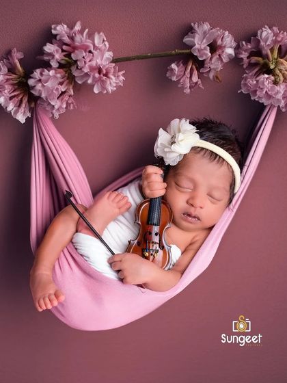 A symphony of sweetness. This newborn girl, nestled in a pink sling with a tiny violin, looks like a little cherub. The floral accents complete this delicate and artistic composition.